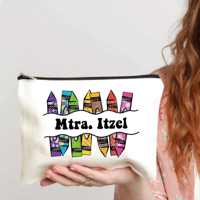 A beige canvas makeup bag with a zipper and black text reading Mtra. Itzel is held by a person with long brown hair.