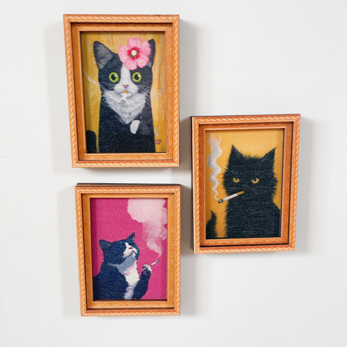 Tres ilustraciones enmarcadas de gatos en blanco y negro con flores rosas y fumando cigarrillos.