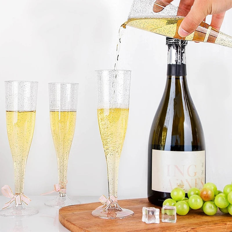 A hand pours sparkling yellow liquid into a clear plastic champagne flute with stem.