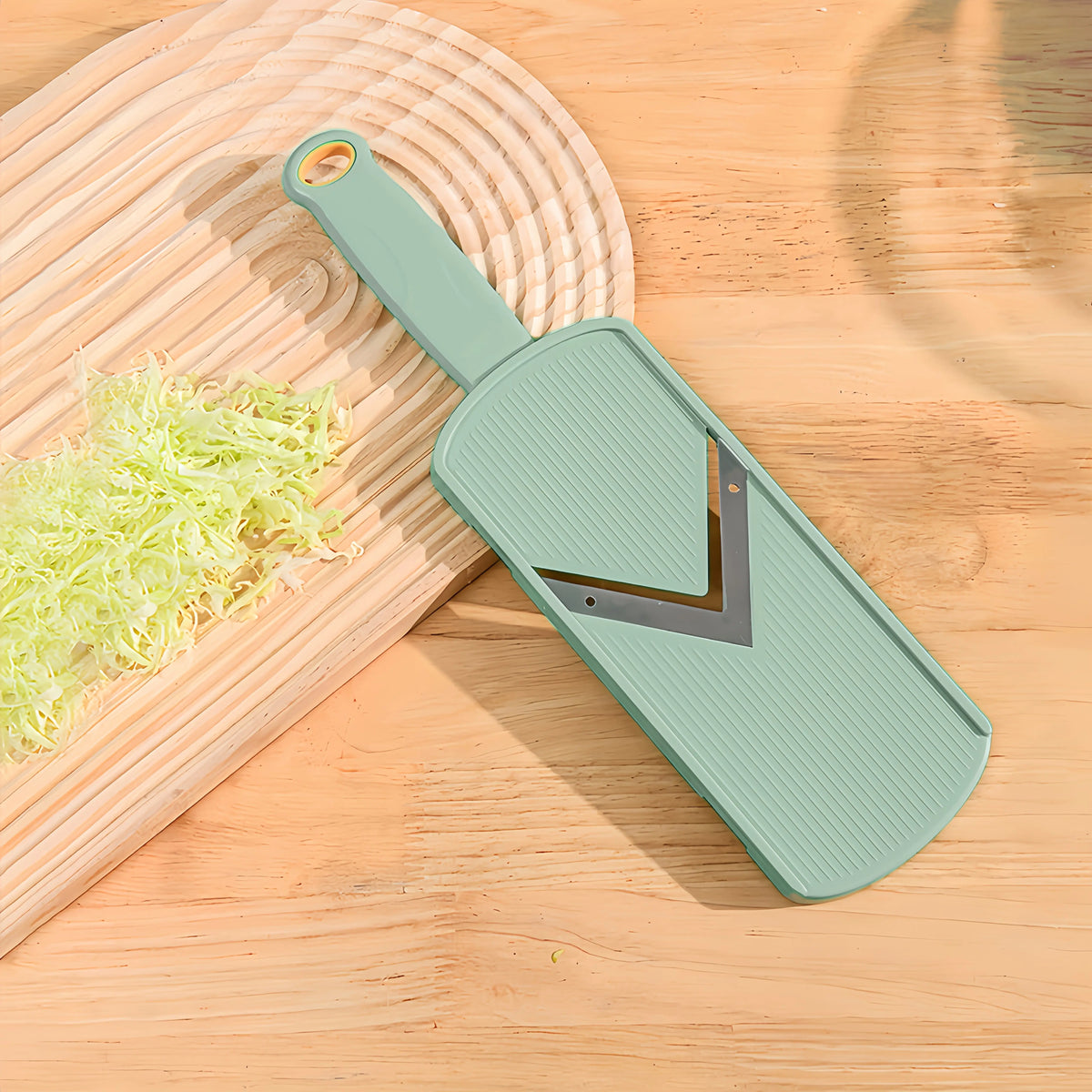 A light green manual cabbage shredder with a wooden handle and stainless steel blades resting on a wooden cutting board.
