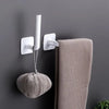 White adhesive cap holder hooks mounted on a gray wall, holding a knitted hat.
