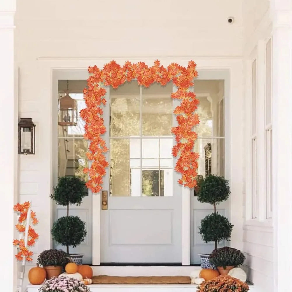 An orange maple leaf garland hangs over a white door frame with potted greenery and seasonal decor.
