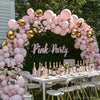 A floral arch made of pink latex balloons decorated with greenery and gold accents for a party backdrop.