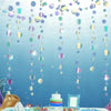 Iridescent mermaid and jellyfish party streamers hanging against a blue background with a cake display.