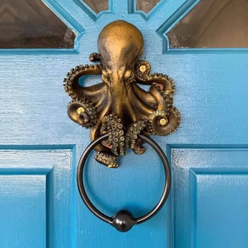 A brass octopus skull door knocker with a cast iron ring mounted on a light blue wooden door.
