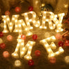 Warm white LED alphabet letter lights spelling out MARRY ME with red and gold ornaments.