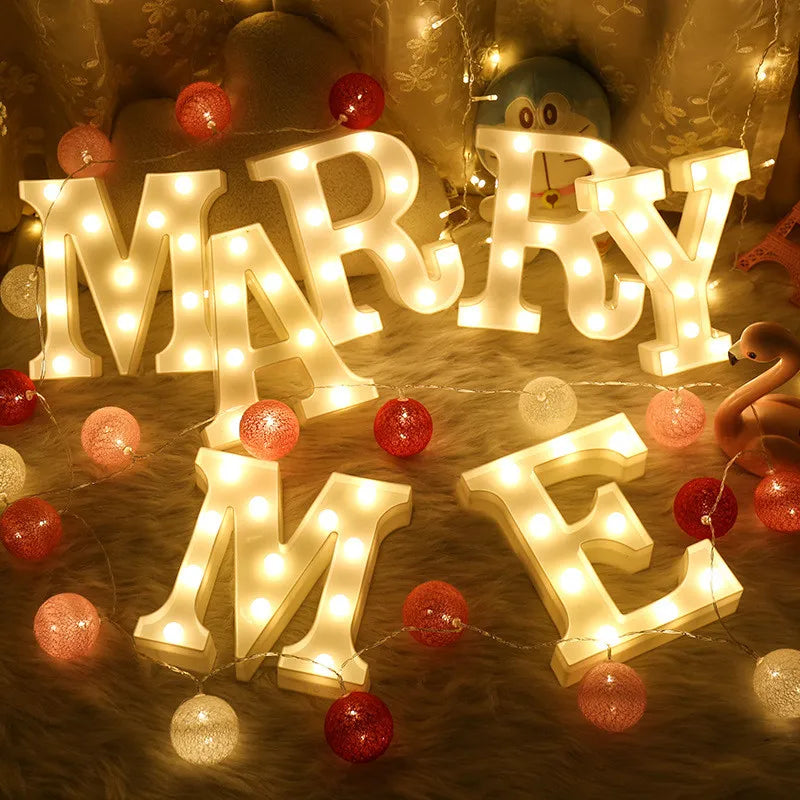 Warm white LED alphabet letter lights spelling out MARRY ME with red and gold ornaments.