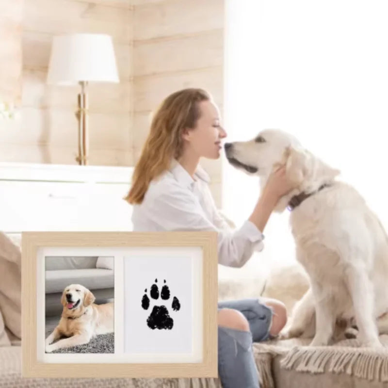 A woman is holding a DIY wooden photo frame kit with pet paw prints and an ink pad, next to a dog.