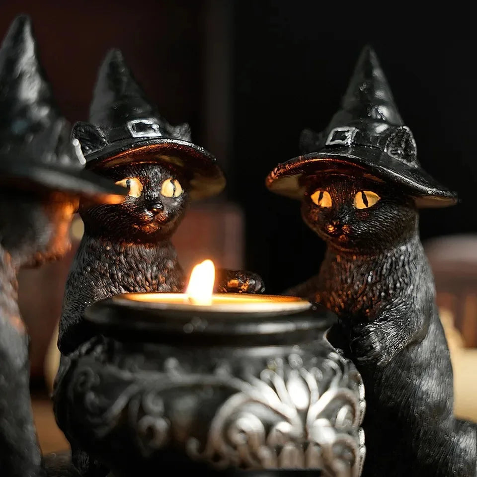 A pair of black cat-shaped witch hats with glowing yellow eyes sitting behind a candle holder.