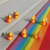 A set of mini resin colorful duck decorations arranged on a rainbow-colored surface.