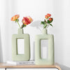 A pair of light green geometric ceramic vases holding orange and pink roses on a wooden surface.