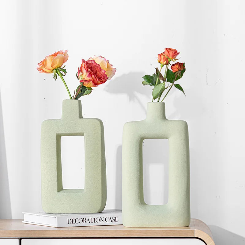 A pair of light green geometric ceramic vases holding orange and pink roses on a wooden surface.