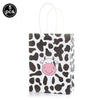 A white paper bag featuring a black and white cow print design with a pink face.