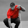 Black and white photo of Tiger Woods in a red shirt crouching on a golf course.