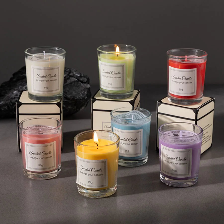 A collection of five scented candles in glass jars with black and cream labels displayed on a gray surface.