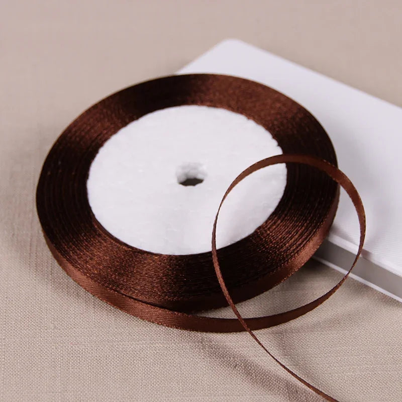 A dark brown satin ribbon spool with a white center is placed on a light beige surface.