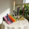 A display of colorful honeycomb beeswax candles and a decorative figurine on a white tablecloth.