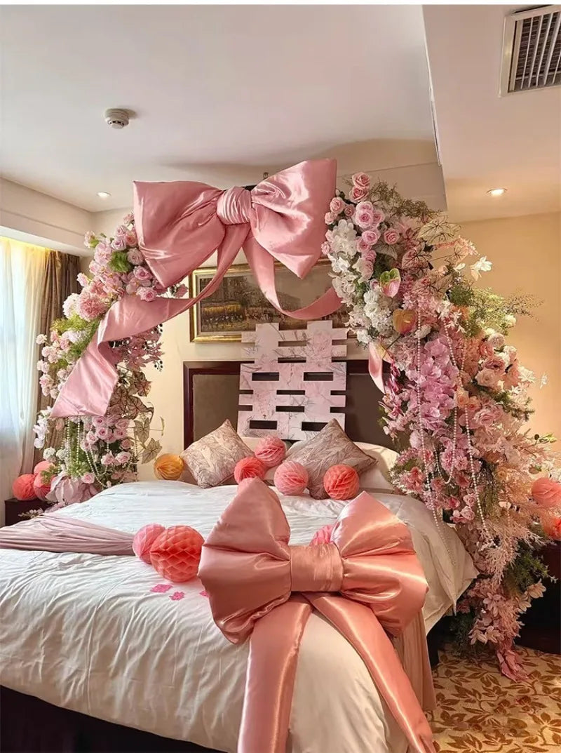 A pink satin bow with long tulle drape decorates a bed with floral arrangements for an event.