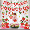 A strawberry theme birthday party decoration set featuring banners, ornaments, and floral accents on a white table.