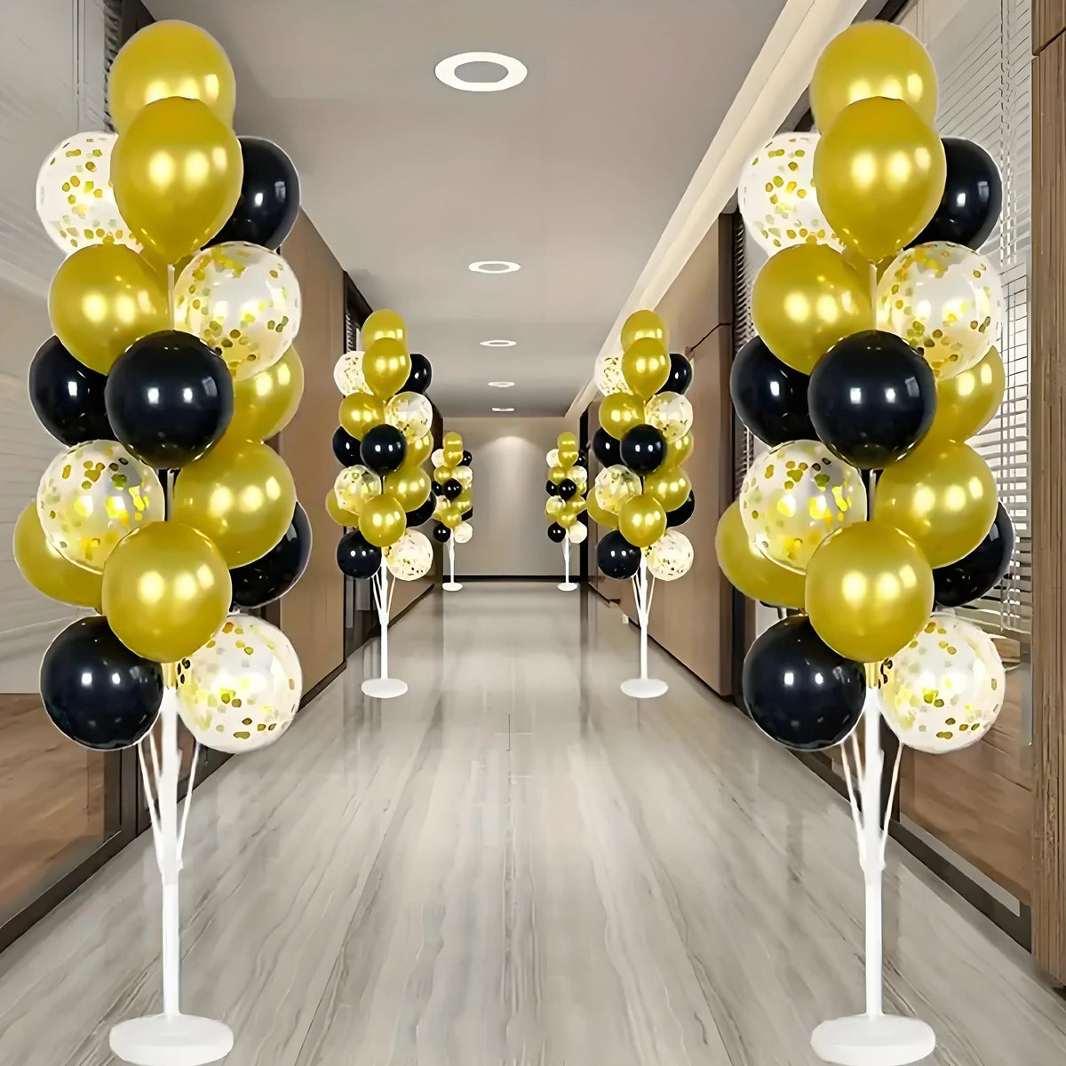 A display of gold and black balloons arranged in tall columns on white stands.