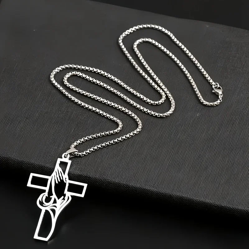 Silver hollow prayer hands cross pendant necklace displayed on a black surface.