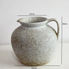 A speckled, round ceramic vase with a handle and spout, shown against a white background.
