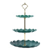 A two-tier serving stand with a gold-toned metal frame and two shallow, scalloped green ceramic plates.