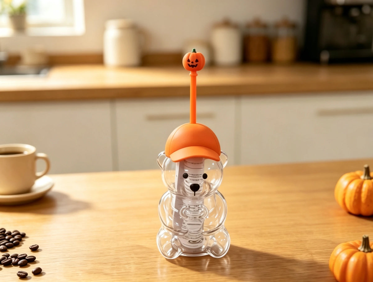 An orange glass coffee cup with a pumpkin-shaped handle is displayed on a wooden table.