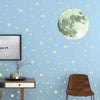 A light blue wall decorated with yellow stars and a large pale green moon decal.