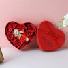 A red heart-shaped gift box filled with artificial red roses and a white plush bear.