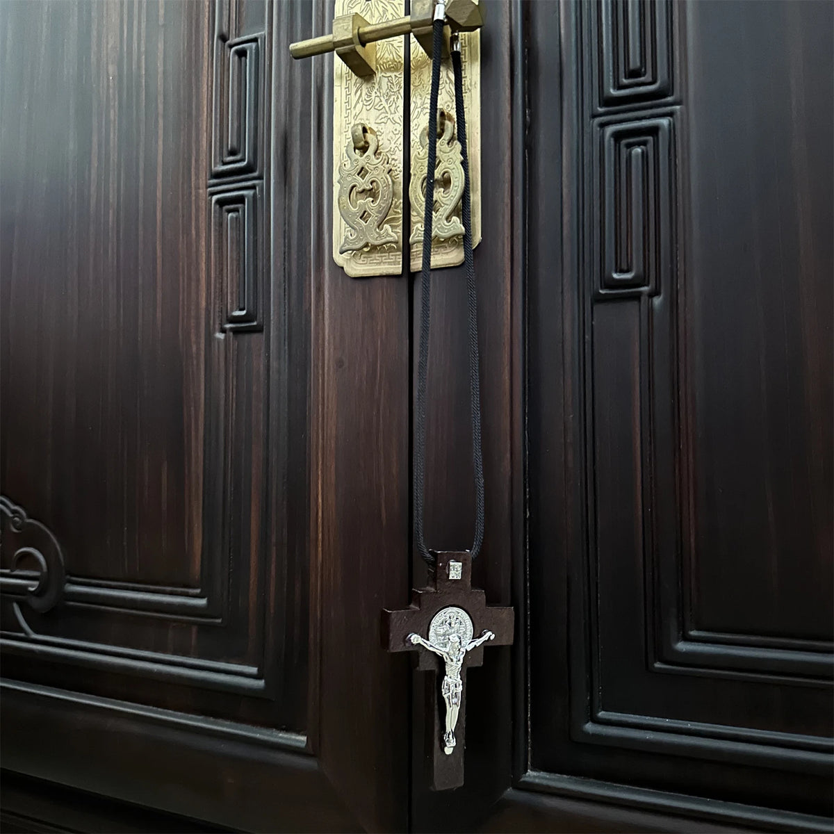A wooden St. Benedict crucifix rosary with a rearview mirror hanger hanging on a dark wood cabinet.