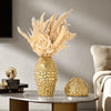 A golden wrinkle ceramic tabletop vase with dried floral arrangements sits on a marble table.