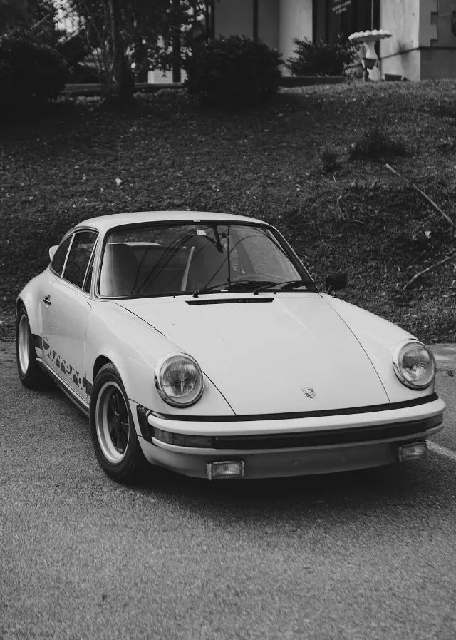 Une Porsche 911 blanche garée sur une route goudronnée avec de la verdure en arrière-plan.