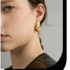 A close-up of a woman's ear showing a gold geometric stud earring.
