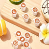 A set of ten miniature white coffee mugs filled with latte art are arranged on a wooden board next to a lemon slice and a pas