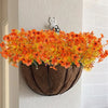 An artificial autumn bouquet of vibrant orange and yellow silk flowers displayed in a brown planter on a white wall.