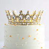 Gâteau à étages blanc décoré d'une couronne en cristal doré et de perles oranges éparpillées.