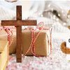 A brown crochet doll with a white headband and an encouragement card sits in front of a wooden cross and wrapped gifts.