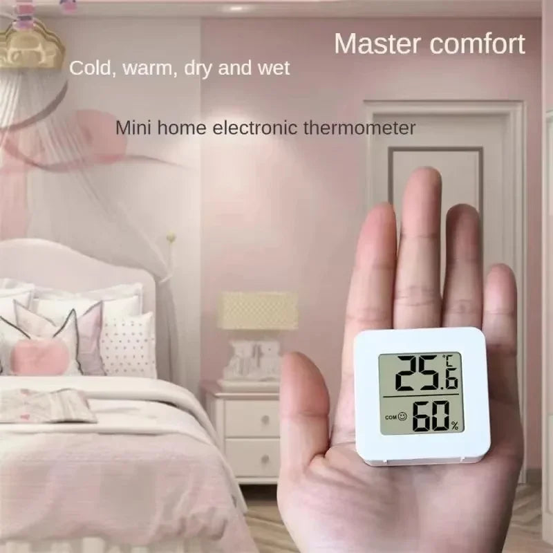 A hand holds a white digital thermometer and hygrometer device in a bedroom setting.