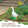 A white goose garden statue with an orange beak and green feet planted in a garden bed.