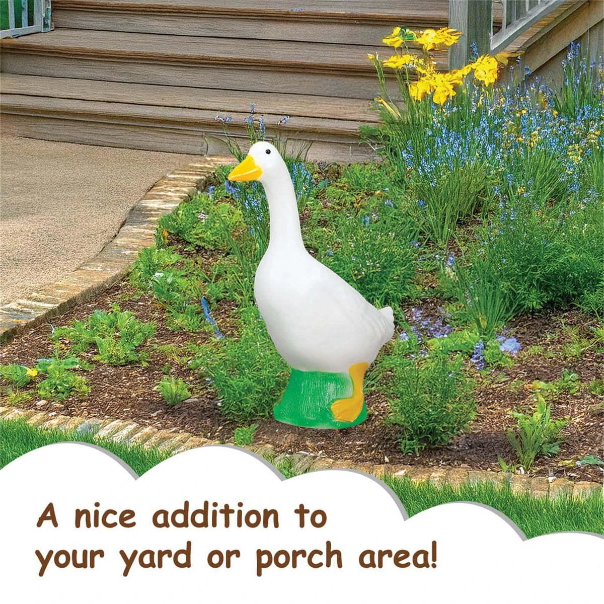 A white goose garden statue with an orange beak and green feet planted in a garden bed.