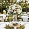 A centerpiece featuring a clear glass cylinder vase filled with greenery and roses on a white table.