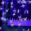 A string of glowing butterfly lights hangs against a dark blue background with green foliage.