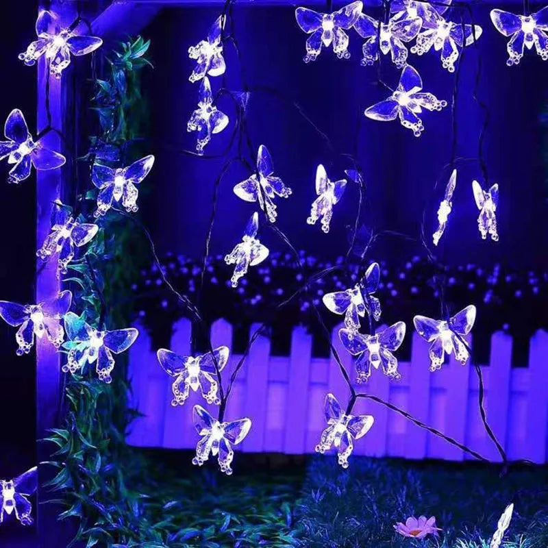 A string of glowing butterfly lights hangs against a dark blue background with green foliage.