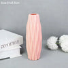 A tall, pink, ribbed plastic vase is shown next to white flowers on a gray background.