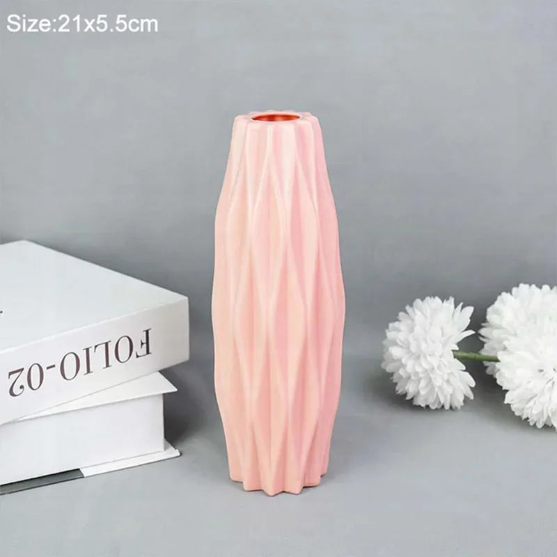 A tall, pink, ribbed plastic vase is shown next to white flowers on a gray background.