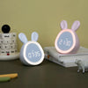 A pink rabbit-shaped mini LED cartoon alarm clock night light resting on a stack of calendar pages.