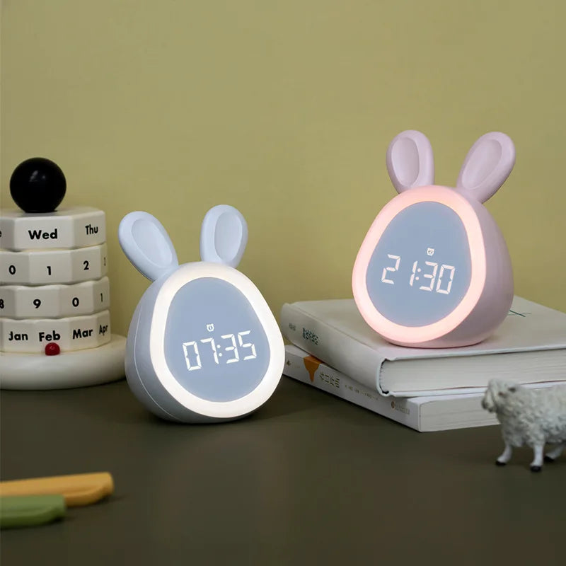 A pink rabbit-shaped mini LED cartoon alarm clock night light resting on a stack of calendar pages.