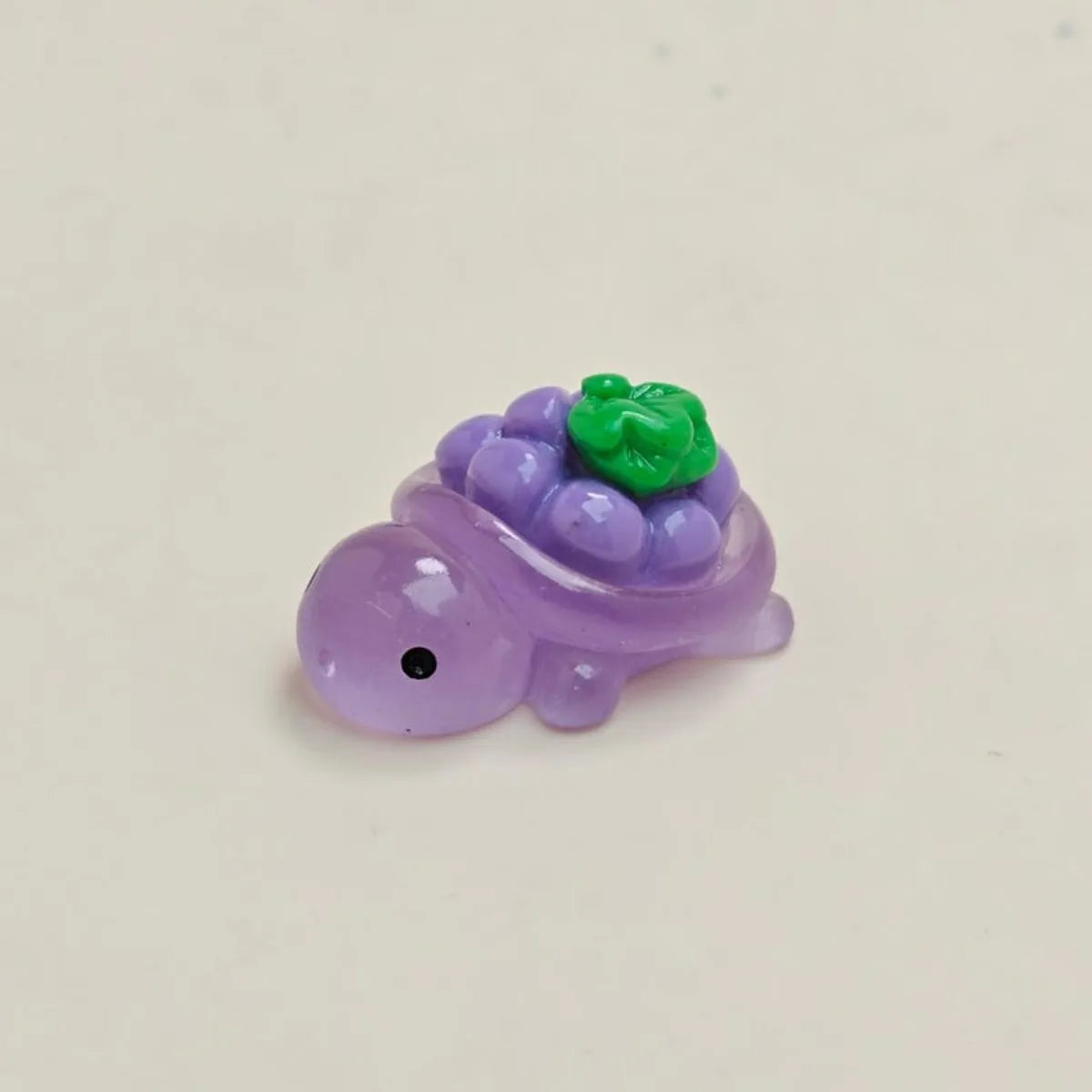 A small purple resin charm shaped like a turtle with green fruit on its back.