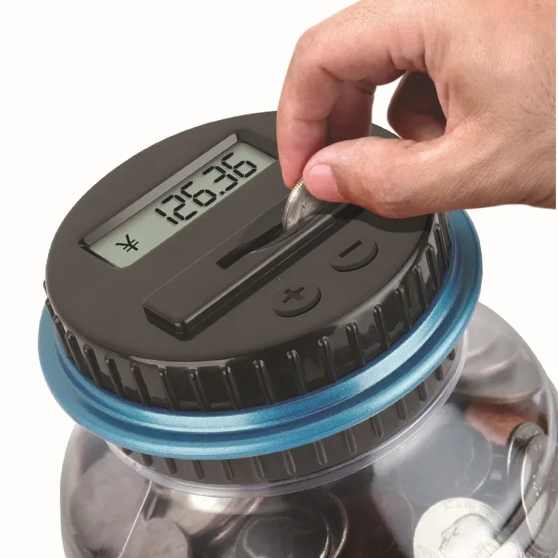 A hand is operating a digital coin counting piggy bank with an LCD display on the top.